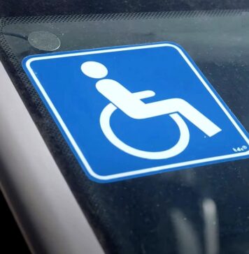 Samochód dla niepełnosprawnego. Zbliżenie na szybę samochodu. W centrum ujęcia niebieska naklejka z symbolem niepełnosprawności.