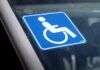Samochód dla niepełnosprawnego. Zbliżenie na szybę samochodu. W centrum ujęcia niebieska naklejka z symbolem niepełnosprawności.