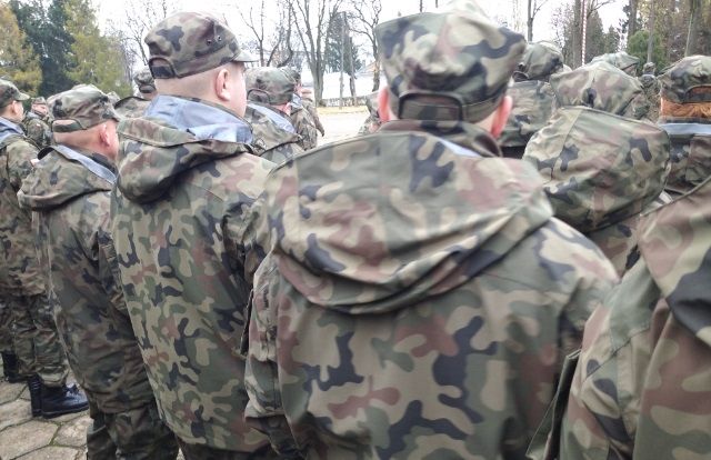Ćwiczenia rezerwy 2022 cz.2 Na zdjęciu liczna grupa mężczyzn. Stoją w sposób niezorganizowany prawdopodobnie na terenie jednostki wojskowej. Wszyscy ubrani w jednakowe stroje w maskujące łaty.