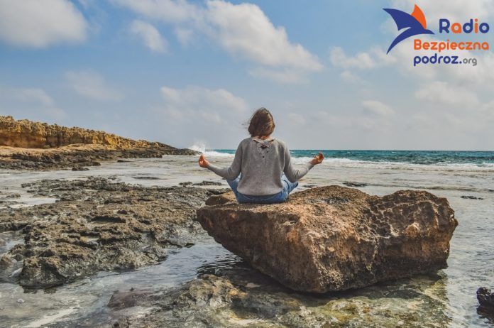Na zdjęciu kobieta siedząca tyłem na skałach na tle morza. Jak się wyciszyć?