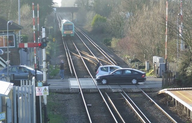 Bezpieczeństwo świątecznych podróży z PLK. Widoczny jest przykładowy przejazd kolejowy. Dwa samochody osobowe, mijają się na środku przejazdu. Do nich zbliża się jadący pociąg.