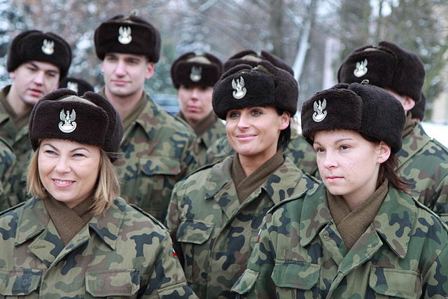 Kwalifikacja wojskowa 2022. Grupa młodych kobiet i mężczyzn w umundurowaniu polowym. Na głowach czarne uszanki ze srebrnym orzełkiem.