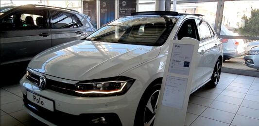 Nowe zasady kupna samochodu od 2023. Na zdjęciu wnętrze salonu sprzedaży samochodów. Na pierwszym planie biały Volkswagen Polo.