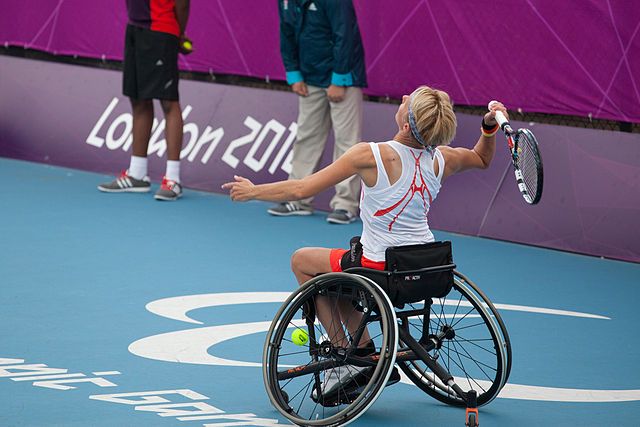 Na zdjęciu zawodniczka na wózku podczas meczu na igrzyskach paraolimpijskich. Tenis ziemny na wózkach.