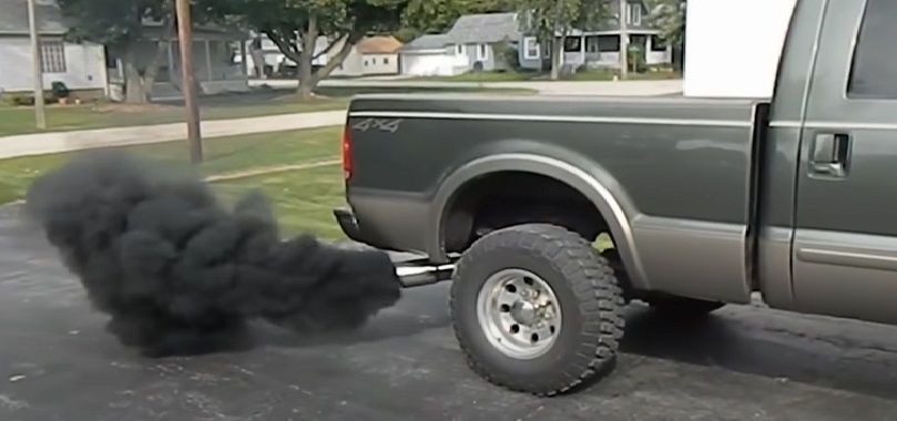 Świece żarowe - czyli jakie. Na podjeździe domu stoi półciężarówka z uruchomionym silnikiem. Z rury wydechowej wydobywają się kłęby czarnego dymu.