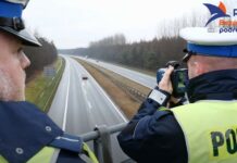 Aktualny taryfikator punktów karnych. Dwaj policjanci drogówki, mierzą prędkość samochodów na autostradzie A1. Pomiaru dokonują stojąc na wiadukcie nad autostradą.