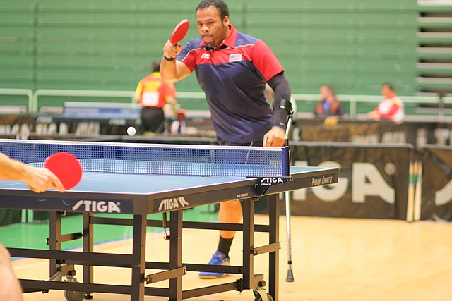 Na zdjęciu niepełnosprawny mężczyzna podpierający się o kuli grający w tenisa stołowego 