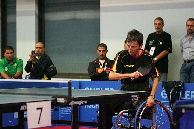 Na zdjęciu mężczyzna na wózku inwalidzkim grający w tenisa stołowego. Tenis stołowy dla osób niepełnosprawnych.