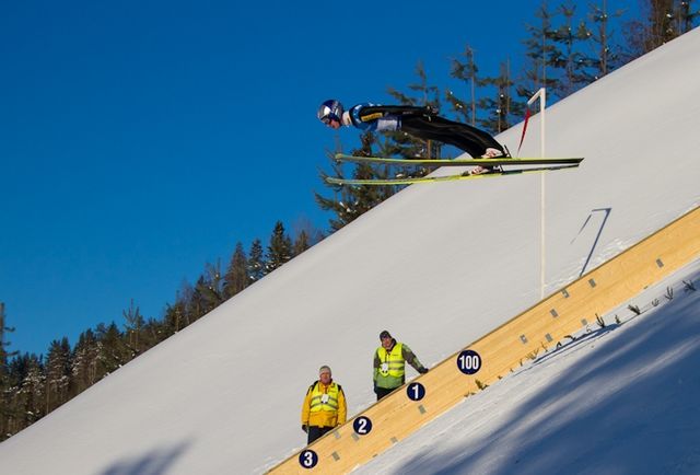 Na zdjęciu Adam Małysz lecący w powietrzu w skoku narciarskim. 