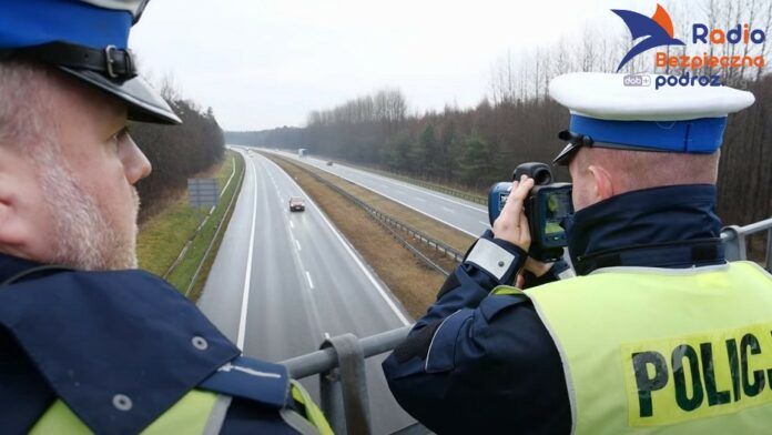 Aktualny taryfikator punktów karnych. Dwaj policjanci drogówki, mierzą prędkość samochodów na autostradzie A1. Pomiaru dokonują stojąc na wiadukcie nad autostradą.