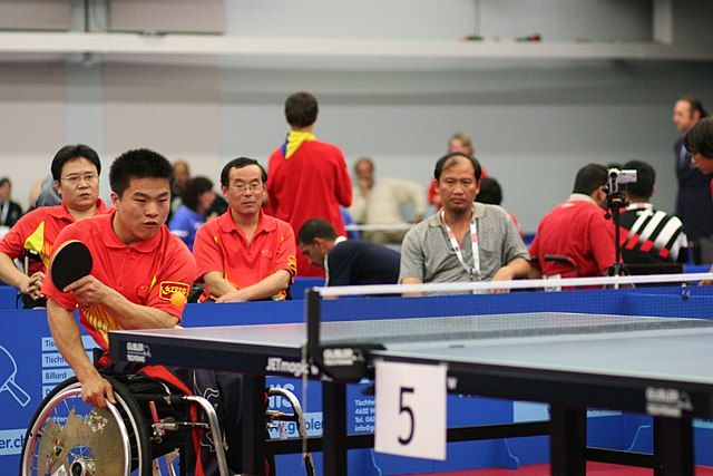 Na zdjęciu niepełnosprawna osoba na wózku grająca w tenisa stołowego.