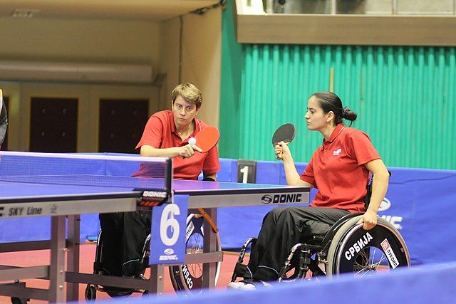 Na zdjęciu zawodniczki na wózkach inwalidzkich grając w tenisa stołowego. Tenis stołowy dla osób niepełnosprawnych.