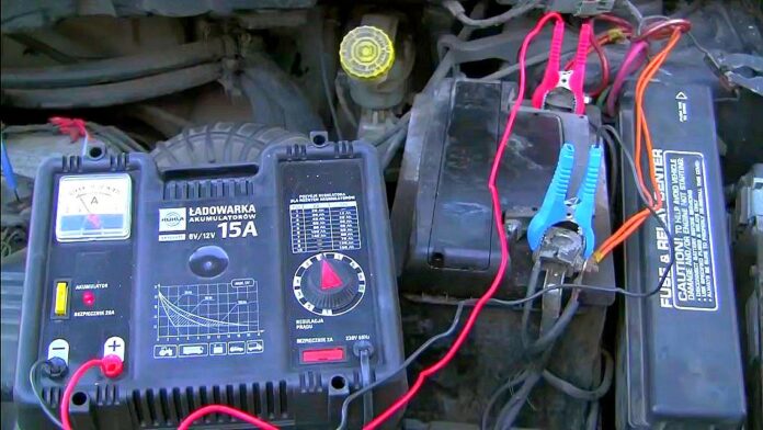 Akumulator rozruchowy - jaki wybrać. Na zdjęciu widoczna komora silnika. W centrum akumulator rozruchowy z podłączoną do niego ładowarką.