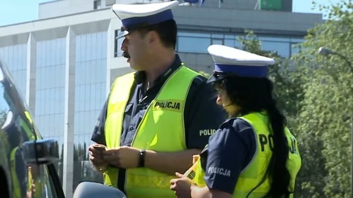 Kontrola drogowa - uprawnienia innych służb. Na zdjęciu dwoje funkcjonariuszy policji, w mundurach drogówki w trakcie kontroli pojazdu.