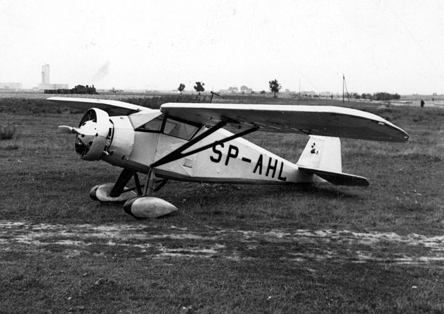 Święto Lotnictwa Polskiego. Stare, biało-czarne zdjęcie z 1932 roku, przedstawia biały, jednoskrzydłowy samolot na trawiastym lotnisku. Jest to właśnie RWD-6 zbudowany w Doświadczalnych Warsztatach Lotniczych w Warszawie.