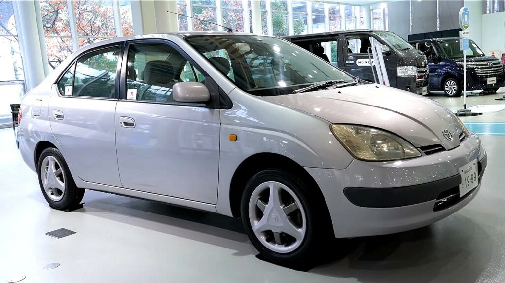 Samochód elektryczny czy hybrydowy - na zdjęciu wnętrze japońskiego komisu samochodowego. W centrum widoczna perłowa Toyota Prius pierwszej generacji.