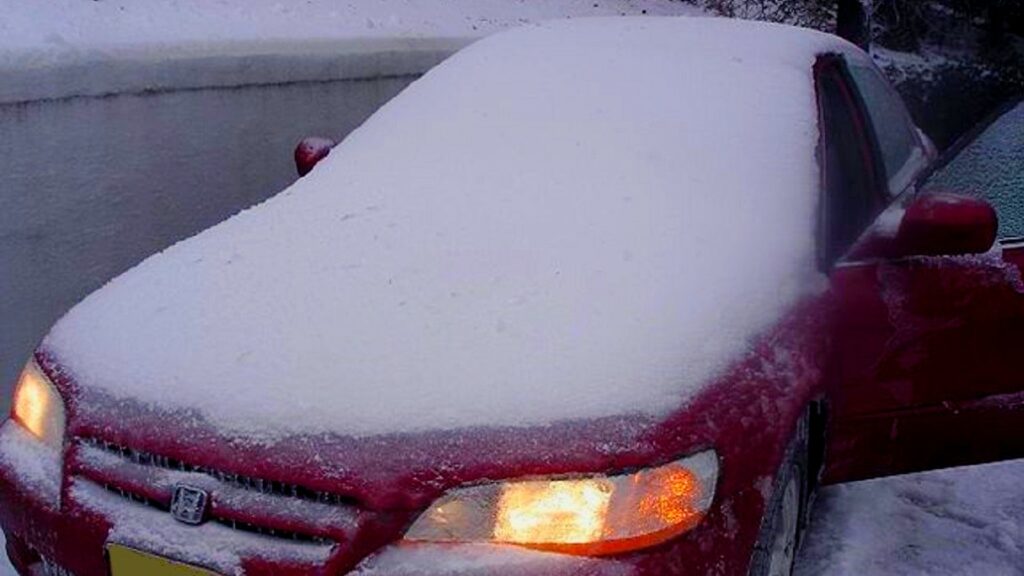 Akumulator rozruchowy - jaki wybrać. Na parkingu stoi czerwona Honda, całkowicie zasypana śniegiem. Otwarte drzwi kierowcy oraz włączone światła.