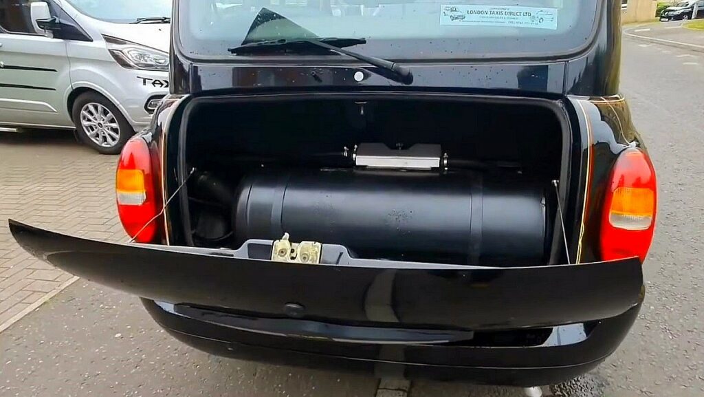 Instalacja LPG w benzyniaku i Dieslu. Otwarty bagażnik londyńskiej taksówki całkowicie wypełnia ogromny zbiornik LPG o kształcie czarnego walca.