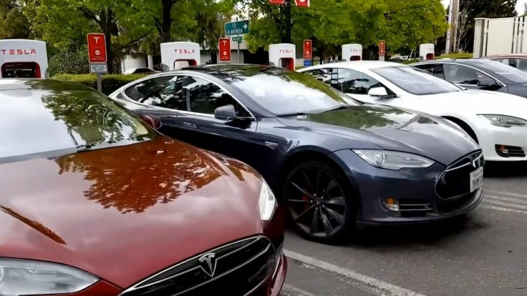 Dopłaty do samochodów elektrycznych. Na zdjęciu parking pełny samochodów Tesla, wszystkie podłączone do ładowarek.