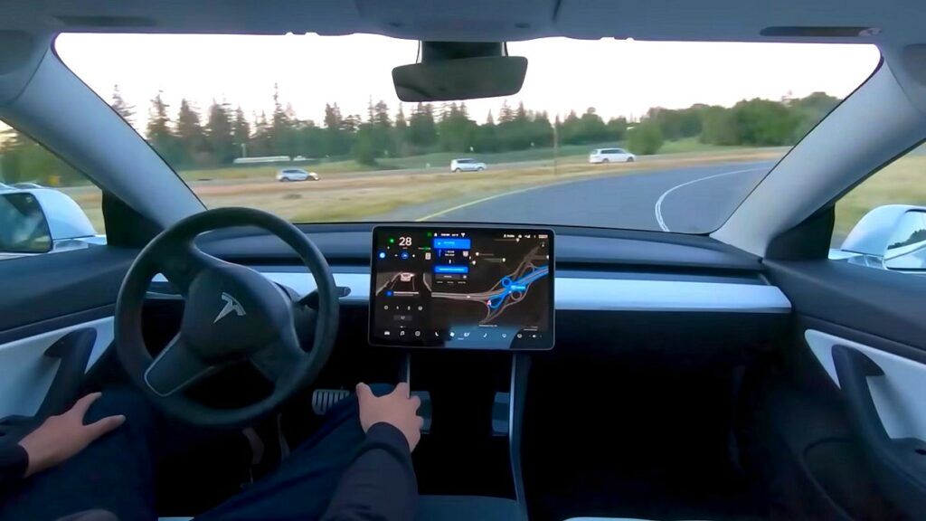 TESLA - wielka akcja serwisowa. Na zdjęciu Tesla jedzie bez pomocy kierowcy. Ten ma ręce położone na kolanach.