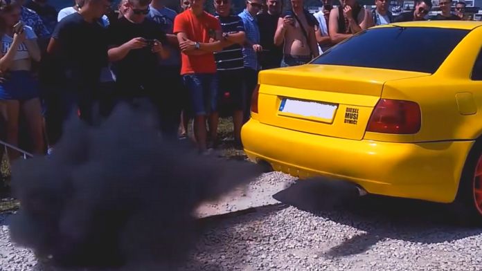 Dym z rury wydechowej - tył żółtego Audi, z rury wydechowej wydobywają się kłęby czarnego dymu