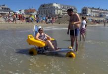 pomysły na wypoczynek osoby niepełnosprawnej. Na francuskiej plaży pan pomaga kobiecie niepełnosprawnej wejść do wody.