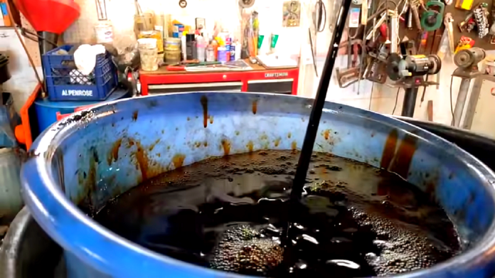 Czarny olej w silniku - na zdjęciu czarny strumień oleju silnikowego leje się do naczynia zlewowego. Odbywa się to w warsztacie pod uniesionym na podnośniku samochodem.