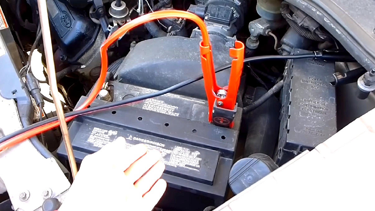 Kable rozruchowe - otwarta klapa silnika, zbliżenie na akumulator. Dodatni, czerwony kabel rozruchowy podpięty do plusa akumulatora, czarny, ujemny do masy pojazdu.