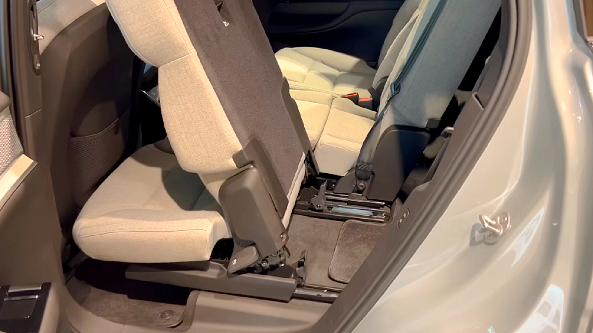 Jasno beżowe wnętrze Volvo EX90. Przez otwarte tylne drzwi pasażera widać uchylony fotel drugiego rzędu siedzeń. Tylko tak można się dostać do trzeciego rzędu foteli.