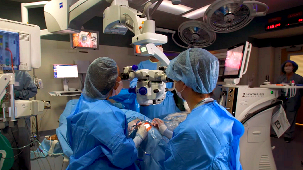 Zaćma - objawy przyczyny leczenie - Na sali operacyjnej dwoje lekarzy usuwa zaćmę. Wokół aparatura, operatorzy w błękitnych fartuchach i czepkach.