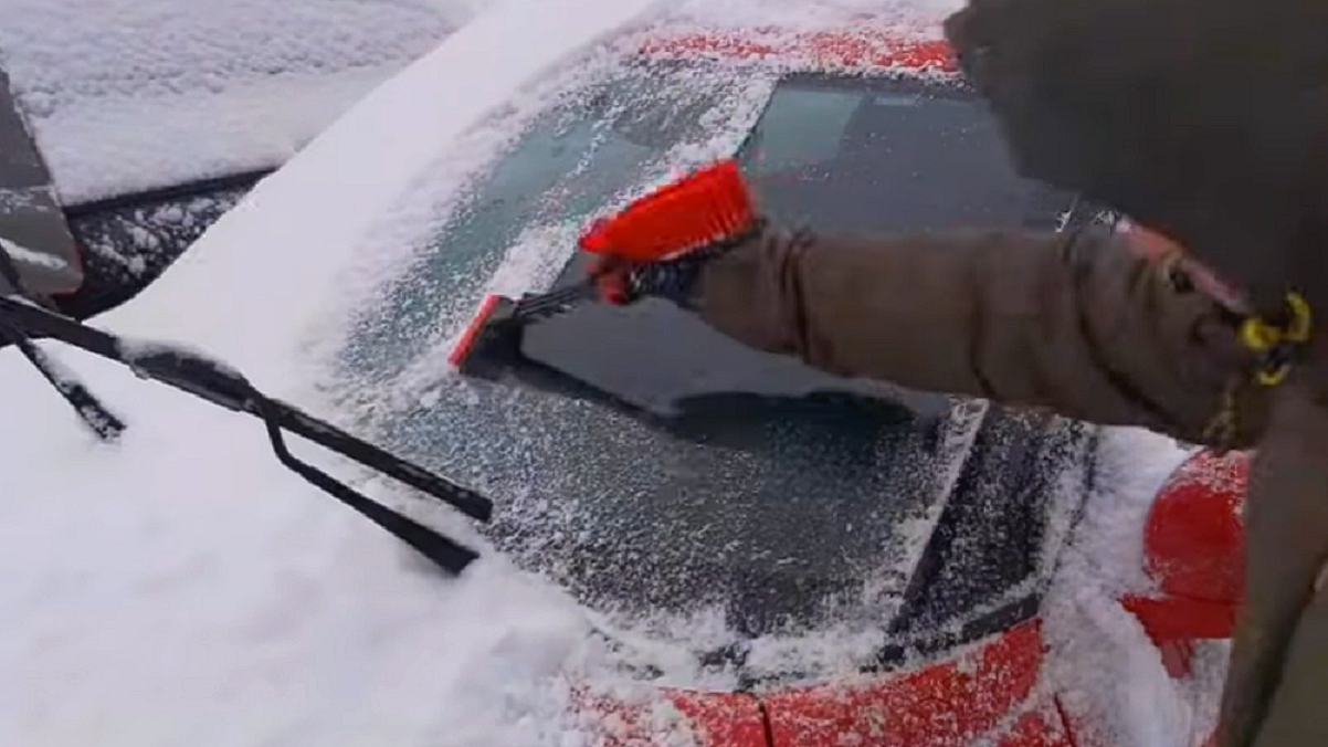 Zamarznięte szyby w samochodzie - kierowca po zmieceniu śniegu, usuwa z szyby lód, z pomocą skrobaczki do szyb.