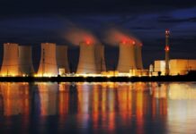 Budowa elektrowni atomowych w Polsce - nocne zdjęci elektrowni atomowej, mocno oświetlone kominy odbijają się na powierzchni wody pobliskiego zbiornika.