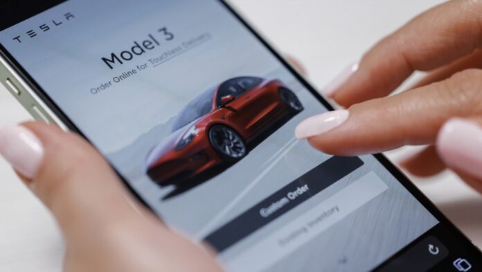Dwa modele Tesli ze zniżką - kobiece dłonie trzymają smartfon, na którym dokonuje zakupu samochodu Tesla Model 3