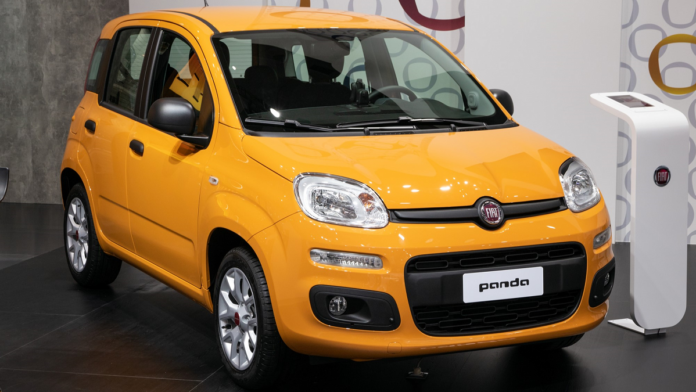 Fiat Panda - nowiutki Fiat Panda Hybrid prezentowany w salonie, na tle białej ściany stoi mocno żółty, lśniący samochodzik.