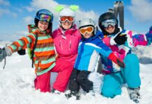 Kask narciarski - na słonecznym i ośnieżonym stoku klęczy cztero-osobowa rodzinka narciarzy i wszyscy mają na głowach kaski