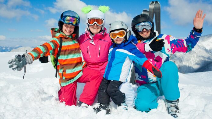 Kask narciarski - na słonecznym i ośnieżonym stoku klęczy cztero-osobowa rodzinka narciarzy i wszyscy mają na głowach kaski