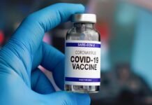 Koncern Pfizer - dłoń w niebieskiej, lateksowej rękawiczce, trzyma fiolkę ze szczepionką na covid-19