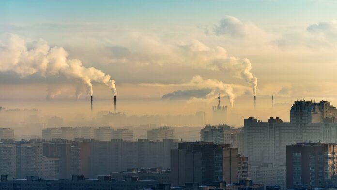 Kraków tonie w smogu - zdjęcie ilustracyjne miasta o wschodzi słońca. Budynki mieszkalne otoczone mgłą i tumanem smogu, w oddali dymiące kominy.