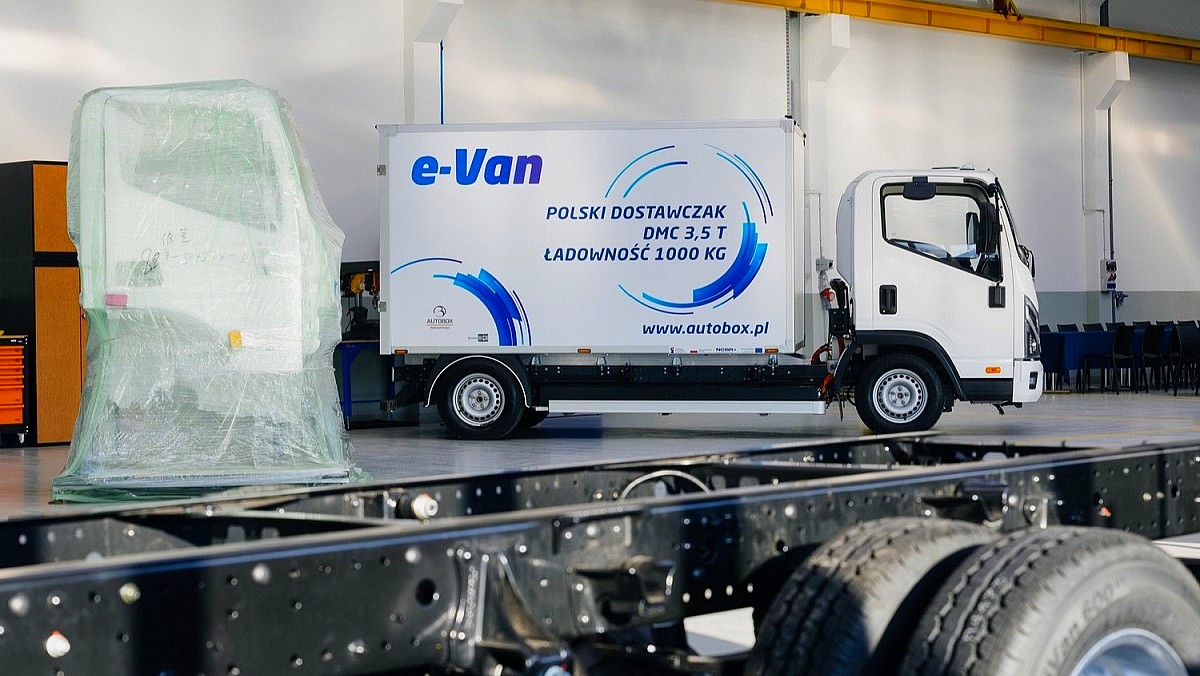 Polski samochód elektryczny - we wnętrzu hali stoi gotowy e-Van w zabudowie kontenerowej. Cały biały, jedynie na burtach błękitne reklamy producenta.