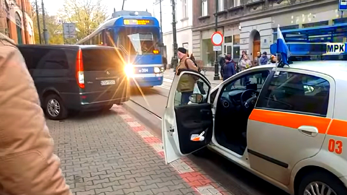 parkowanie na chodniku - na krakowskim chodniku zaparkowany bus marki mercedes, wystajez chodnika i blokuje przejazd niebieskiego tramwaju. Na ulicy zapanował chaos.
