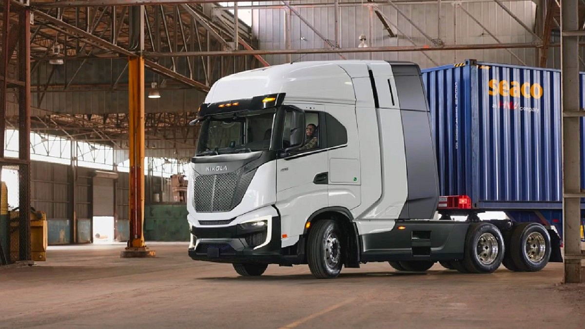 Firma BOSCH - biała ciężarówka Nicola TRE FCEV, wewnątrz hali załadunkowej na naczepie niebieski kontener.