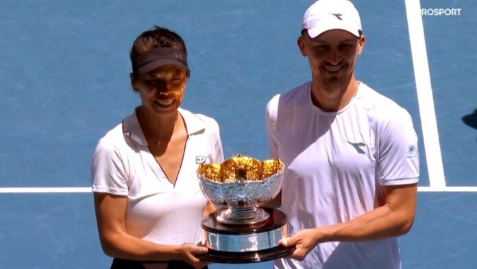Jan Zieliński - zwycięska para tenisistów Jan Zieliński i Su-Wei Hsieh, oboje w białych koszulkach i czapeczkach, trzymają razem puchar Australian Open. W tle niebieska nawierzchnia kortu tenisowego.
