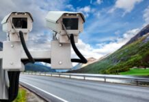 Nowy fotoradar - dwie białe skrzynki fotoradarów umocowane nad autostradą, w oddali górski krajobraz