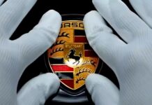 Porsche Taycan - zbliżenie na dłonie w bawełnianych, białych rękawiczkach, naklejających logo Porsche na masce samochodu.