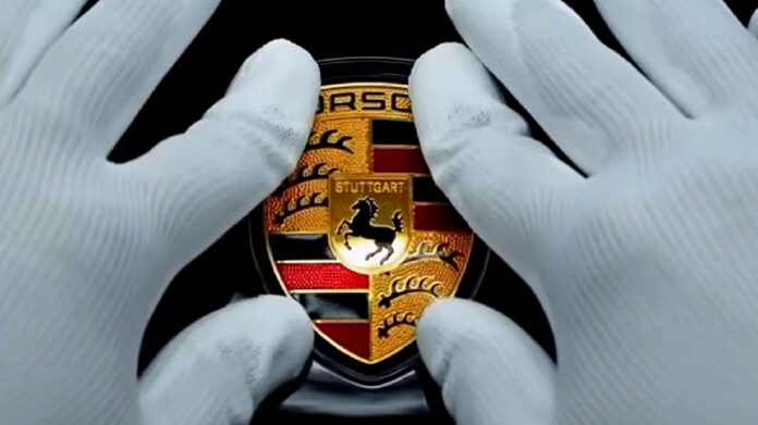 Porsche Taycan - zbliżenie na dłonie w bawełnianych, białych rękawiczkach, naklejających logo Porsche na masce samochodu.