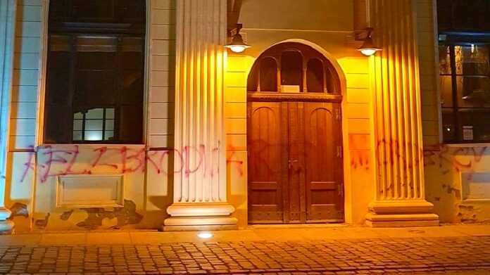 Zbezczeszczenie synagogi - nocne zdjęcie wejścia do synagogi z napisem wykonanym sprayem.