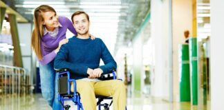 zmiany w przepisach dla niepełnosprawnych, uśmiechnięta kobieta i niepełnosprawny mężczyzna na wózku na korytarzu biurowca