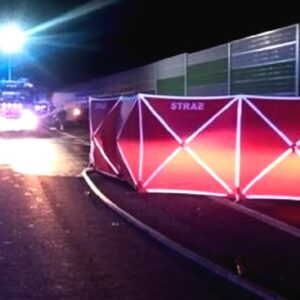 Sebastian M. - nocne zdjęcie z miejsca wypadku. Na zablokowanej autostradzie rozstawiony czerwony parawan z napisem straż, osłaniający ciała ofiar. Obok karetki i wozy strażackie z włączonymi kogutami.