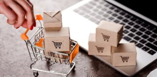 Fabryka Opakowań Kartonowych przegrywa proces Sprzedajesz przez internet - na biurku leży otwarty laptop, na nim piramidka maleńkich, kartonowych pudełeczek z symbolem koszyka zakupowego. Obok laptopa stoi miniatura kosza na czterech kołach, a w nim takie same pudełka.