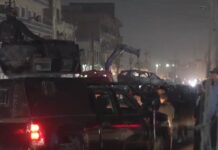atak drona - nocny widok ulicy w Bagdadzie. Tłumy gapiów, policji i wojska. W oddali dźwig podnosi wrak samochodu zniszczonego przez drona.